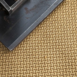 Sol en sisal Slow doré avec tissage naturel et objet décoratif posé au sol