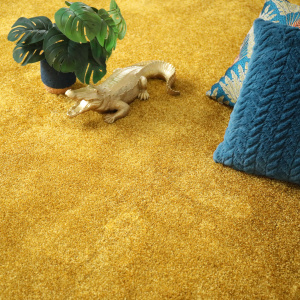 Moquette velours Feelings Balsan jaune Carat 350 à la coupe dans un salon avec coussin bleu et plante
