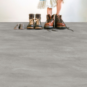 Revêtement PVC Batimax Styx T39 imitation béton, présenté dans un intérieur lumineux avec plusieurs paires de chaussures