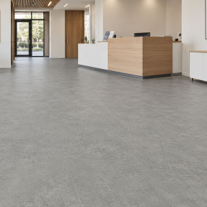 Sol PVC classé U3P3 - IPERFORM 370 - Pinnacles T83, aspect béton gris dans un espace d'accueil contemporain avec comptoir en bois et fauteuils
