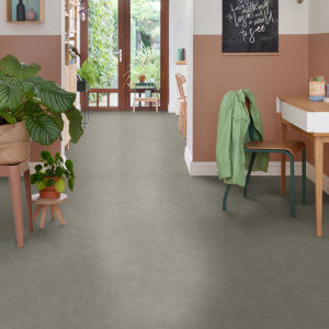 Sol vinyle Batimax Cosmos T91 aspect béton gris dans une pièce de vie lumineuse avec plantes vertes, mobilier en bois et chaises vertes