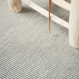 Moquette tissé plat Nusa Blanc craie avec pied de meuble bois et texture en petites boucles