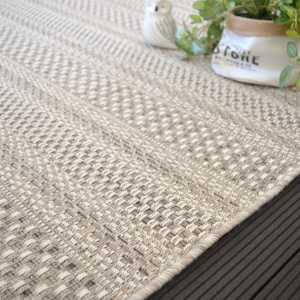 Salon extérieur cosy avec tapis Indy grège, mobilier bois et coussins beiges