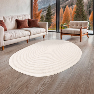 Tapis Circle cercle crème de forme ovale organique, posé dans un salon chaleureux avec vue montagne