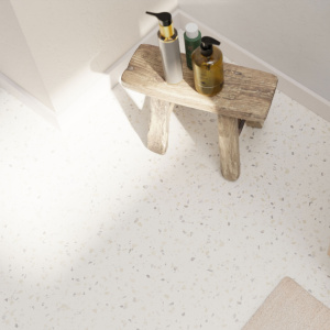 Sol vinyle Prestige Batitec - Coronet T10 aspect terrazzo clair dans une salle de bain lumineuse avec tabouret en bois et accessoires