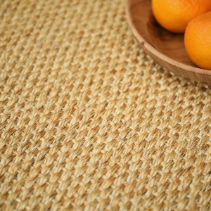 Zoom sur la texture du tapis en sisal Tulum coloris miel avec assiette en bois et fruits oranges