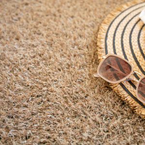 Détail gazon synthétique Essential Garden 22 mm beige sable avec lunettes et chapeau, ambiance été