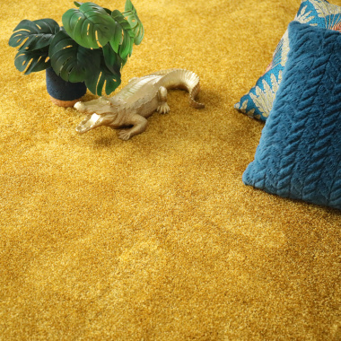 Moquette velours Feelings Balsan jaune Carat 350 à la coupe dans un salon avec coussin bleu et plante