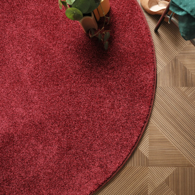 Tapis rond rouge passion en velours posé dans un salon, finition soignée et contraste avec le sol graphique
