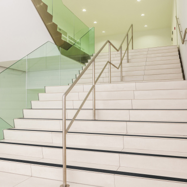 Escalier large en pierre claire équipé de bandes antidérapantes noires sur les nez de marche