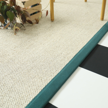 Tapis en sisal Tulum blanchi avec ganse vert émeraude, vue en perspective avec fauteuil et décor végétal