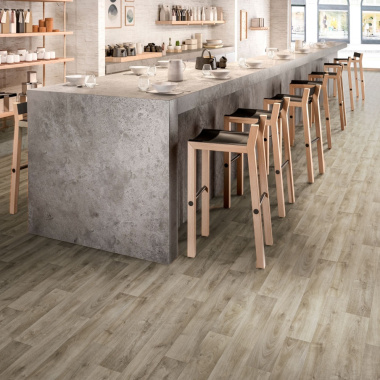 Sol vinyle Prestige Batitec - Tavel T31, imitation parquet bois grisé dans un espace de restauration avec comptoir et tabourets hauts