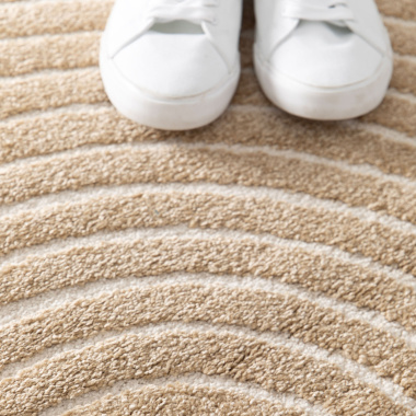 Zoom sur les reliefs du tapis Circle Courbe beige et crème sous des baskets blanches