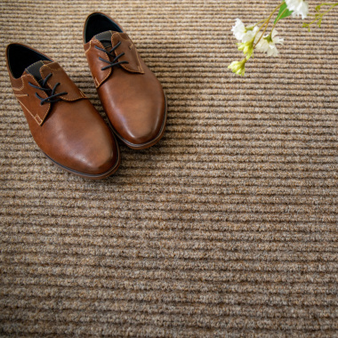 Tapis d’entrée beige, ambiance déco avec chaussures marron et vase blanc