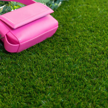 Gazon synthétique Nomade - 34 mm - À raccord scratch, pelouse verte avec sac rose posé près d'un massif de fleurs