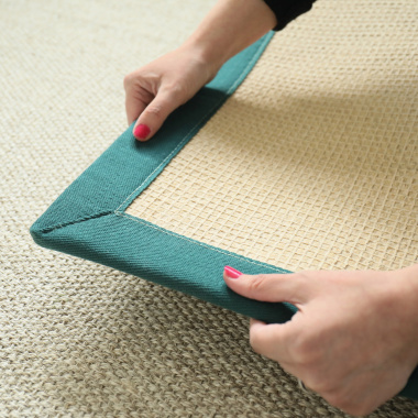 Zoom sur l’envers du tapis sur mesure en sisal Tulum blanchi avec ganse vert émeraude, tenu à la main