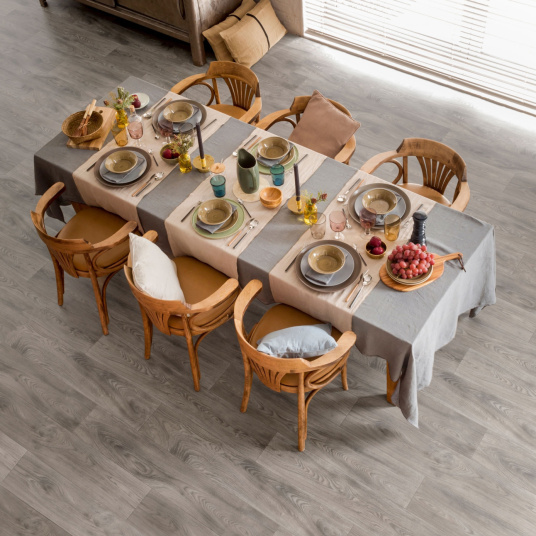 Sol vinyle Prestige Batitec - Burned Wood T94, aspect parquet bois grisé dans une salle à manger avec table dressée et chaises en bois