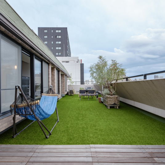 Terrasse moderne aménagée avec du Gazon synthétique Brunch 18 mm et un hamac suspendu, espace détente urbain