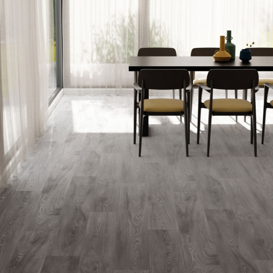 Sol vinyle Prestige Batitec - Burned Wood T94, imitation parquet bois gris dans une salle à manger lumineuse avec grandes fenêtres