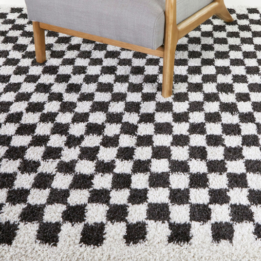 Tapis à damier Colorama noir et blanc à poils longs sous fauteuil en bois