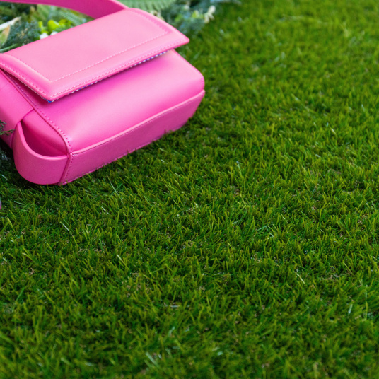 Gazon synthétique Nomade - 34 mm - À raccord scratch, pelouse verte avec sac rose posé près d'un massif de fleurs