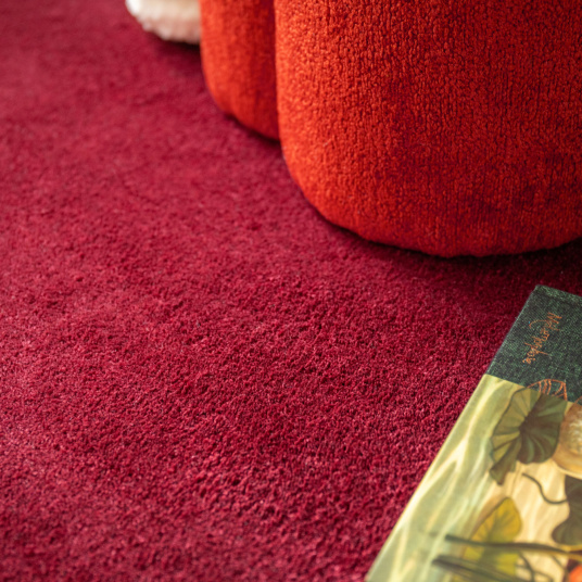 Moquette ultra douce Pulse rouge grenat, texture velours dense avec pouf et livre